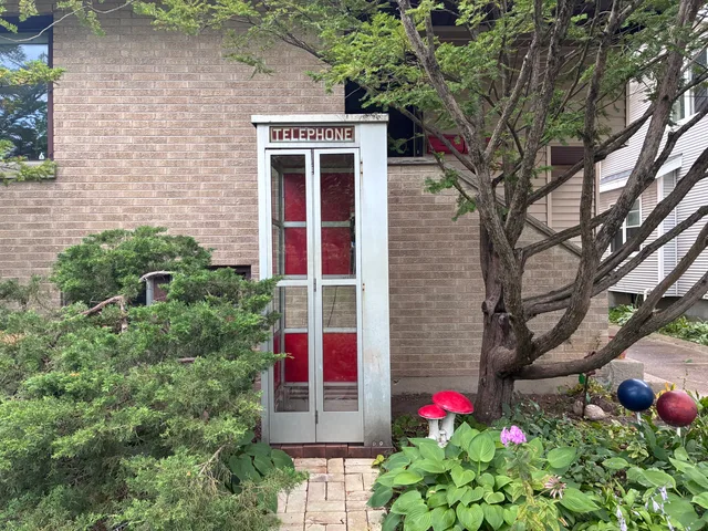 The memorial booth nestled among trees, garden plants and red mushroom sculptures